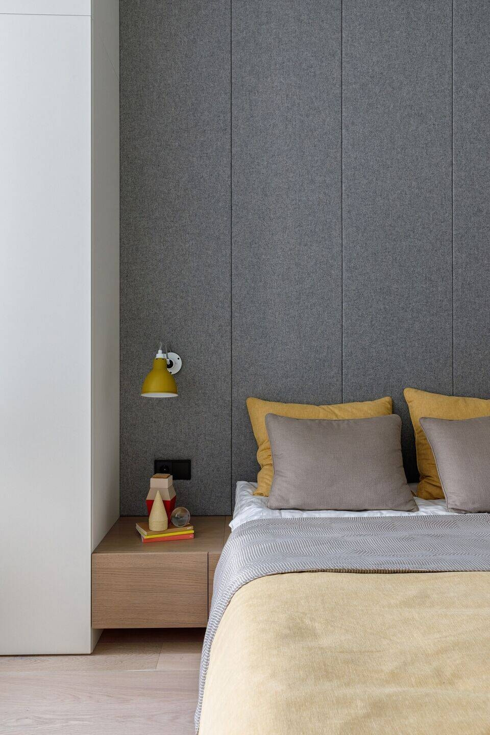 Thiết kế nội thất quận 9 vách đầu giường ốp nỉ xám và gối màu vàng.